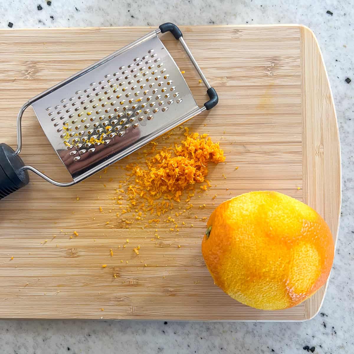 Orange being zested on a cutting board with a micro-plane grater.