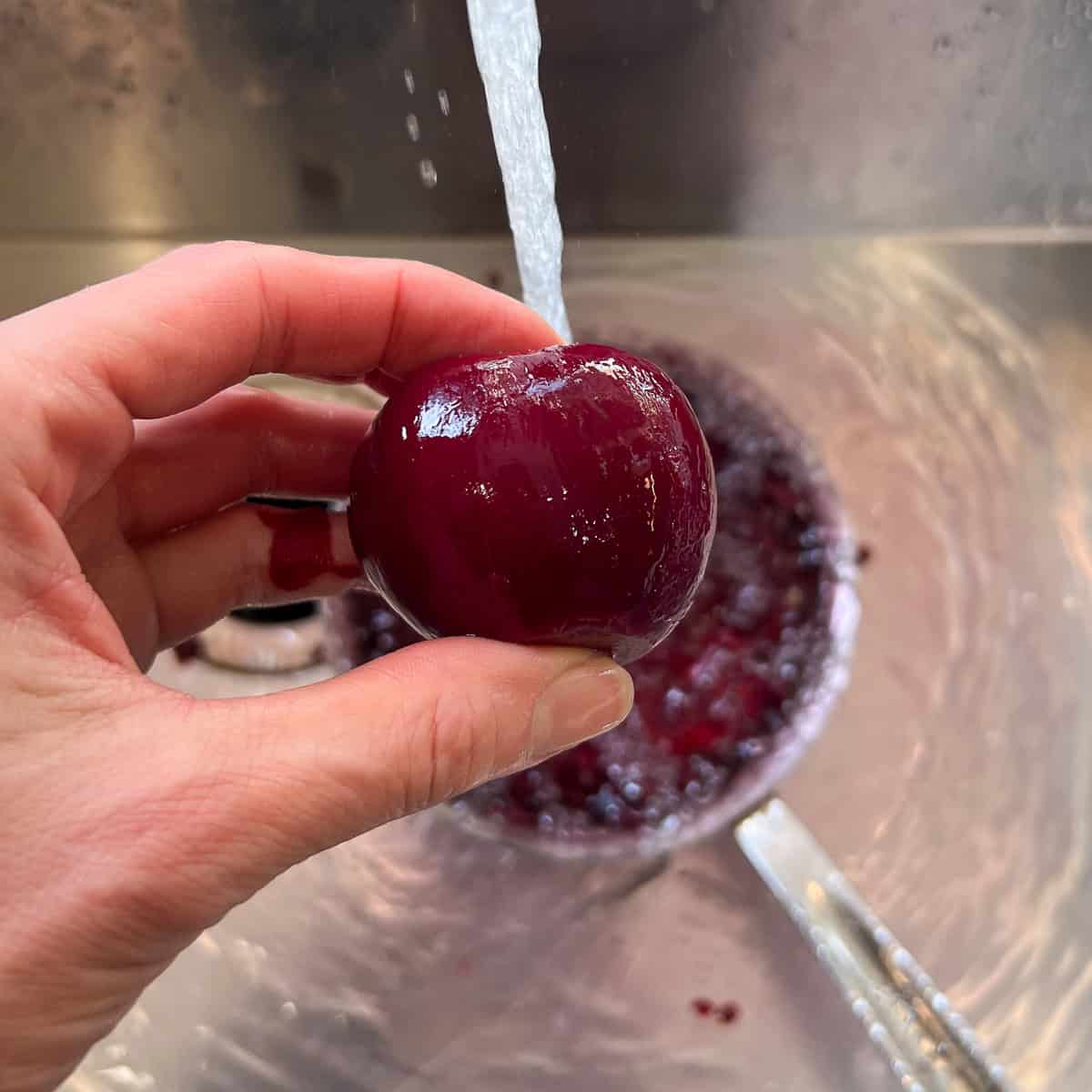 Cooked beets being run under cold water and skin peeled with hands.
