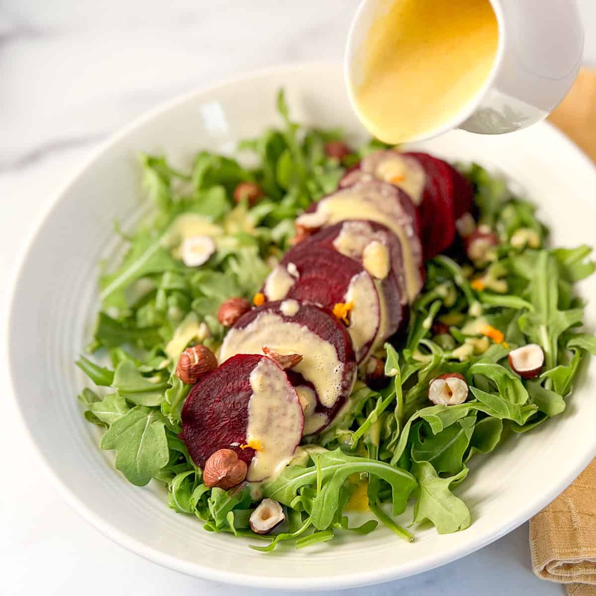 Arugula and beet salad being dressed with orange citrus dressing.