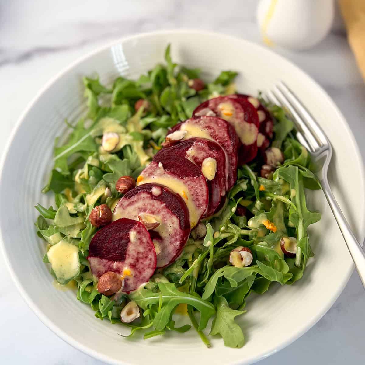 Arugula and beet salad in a bowl with dressing and chopped nuts on top and fork on the side.