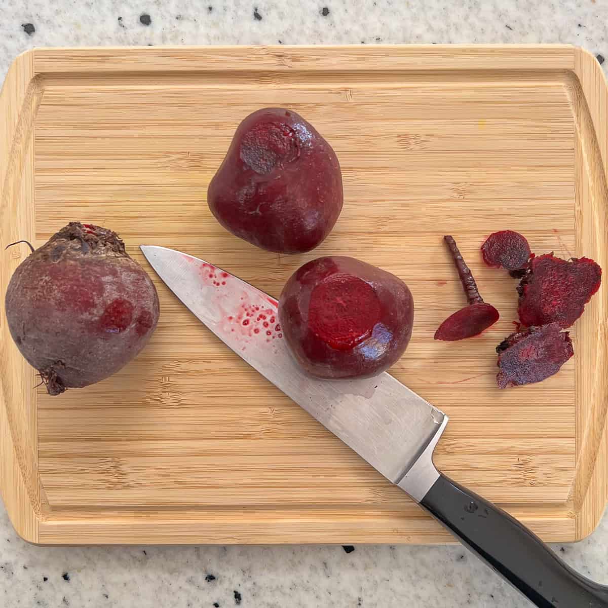 Beets on a cutting board being trimmed with a knife.