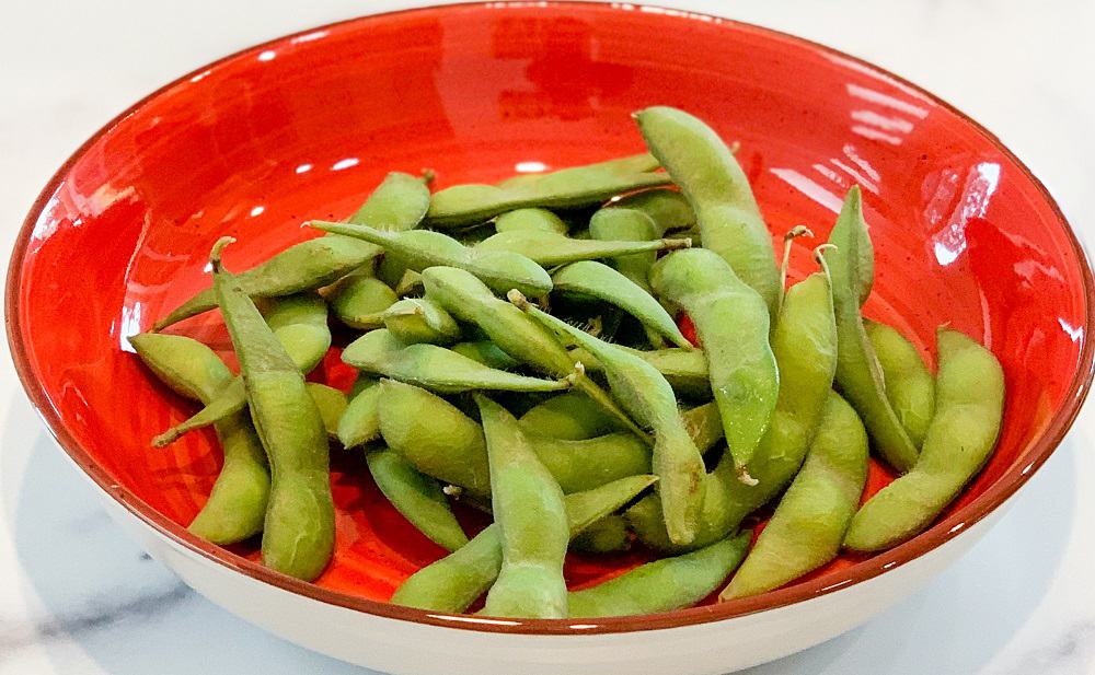 Close up view of cooked edamame in a red bowl 