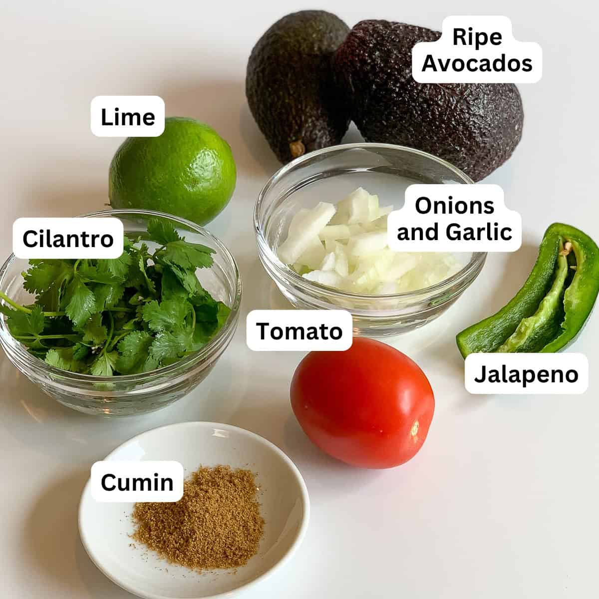 Ingredients for homemade guacamole: avocado, lime, chopped onion, garlic, tomato, jalapeno, cilantro and ground cumin.