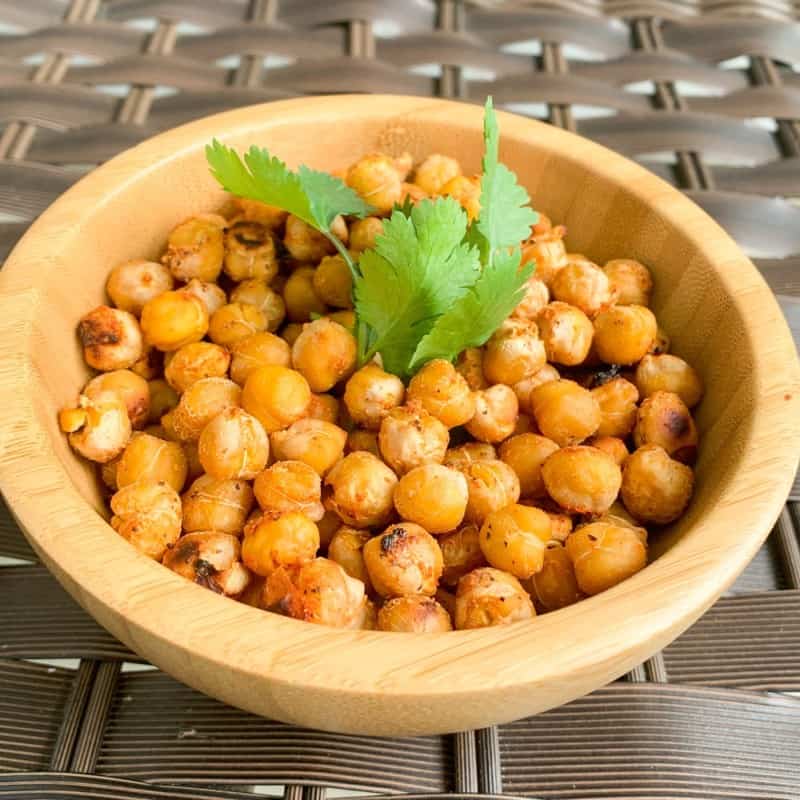 roasted chickpeas in a wooden bowl with a sprig of cilantro on top against a woven background
