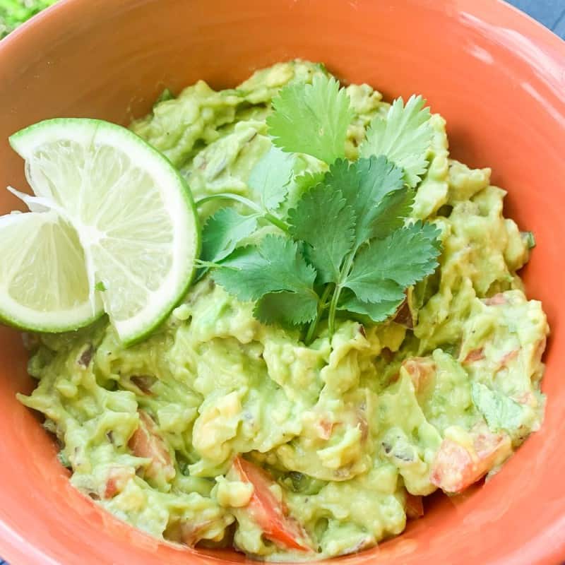a red bowl with guacamole, lime wedges and fresh cilantro
