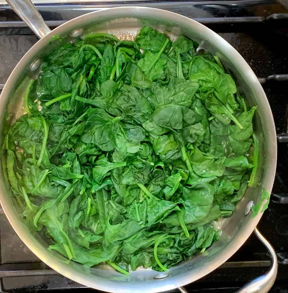 top view close up of fresh spinach being water sautéed on the stovetop in a stainless steel sauté pan