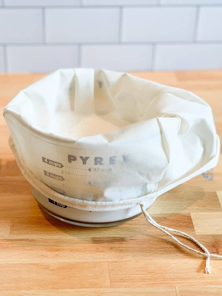 A nut milk bag lining a one quart measuring cup.