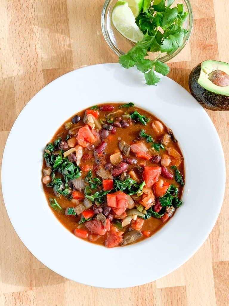 top view close up of ultimate veggie chili in a white bowl with fresh cilantro, lime and avocado on the side