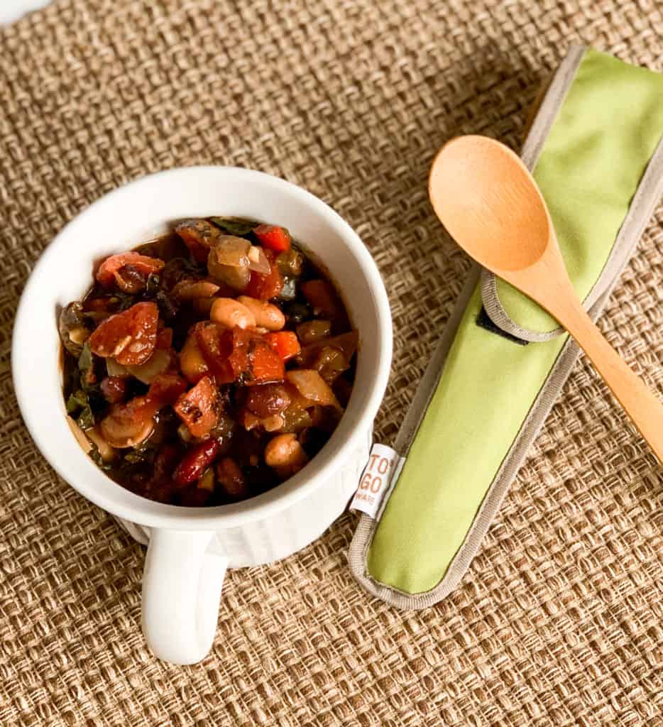 an individual container of veggie chili with a wooden soup spoon