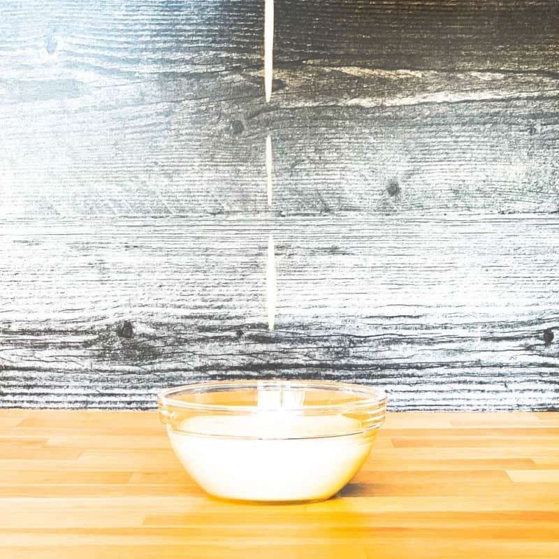 cashew cream sauce being poured into a small glass bowl against a stained wood backdrop