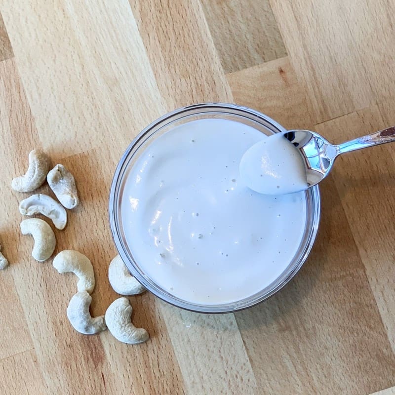 a glass bowl of cashew cream and loose cashews on the left side