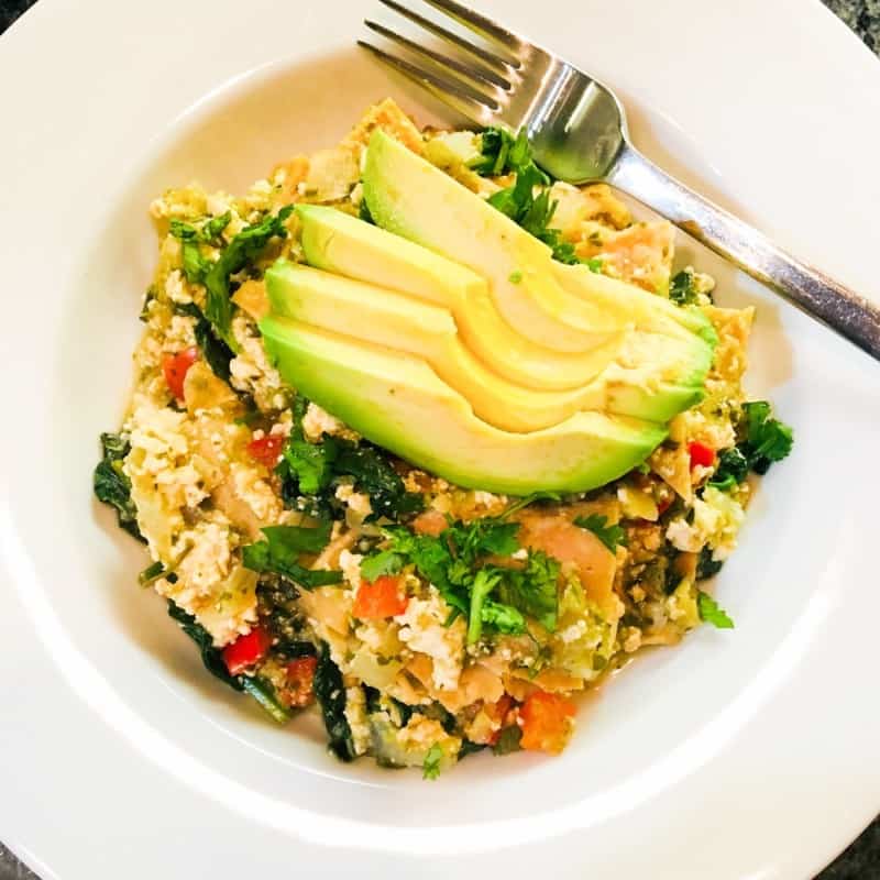 top view close up of veggie tofu scramble chilaquiles with sliced avocado on top and fork on the side