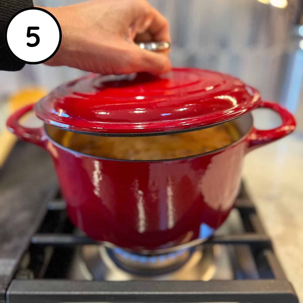 A woman's hand adding the lid to the soup pot to partially cover for cooking.
