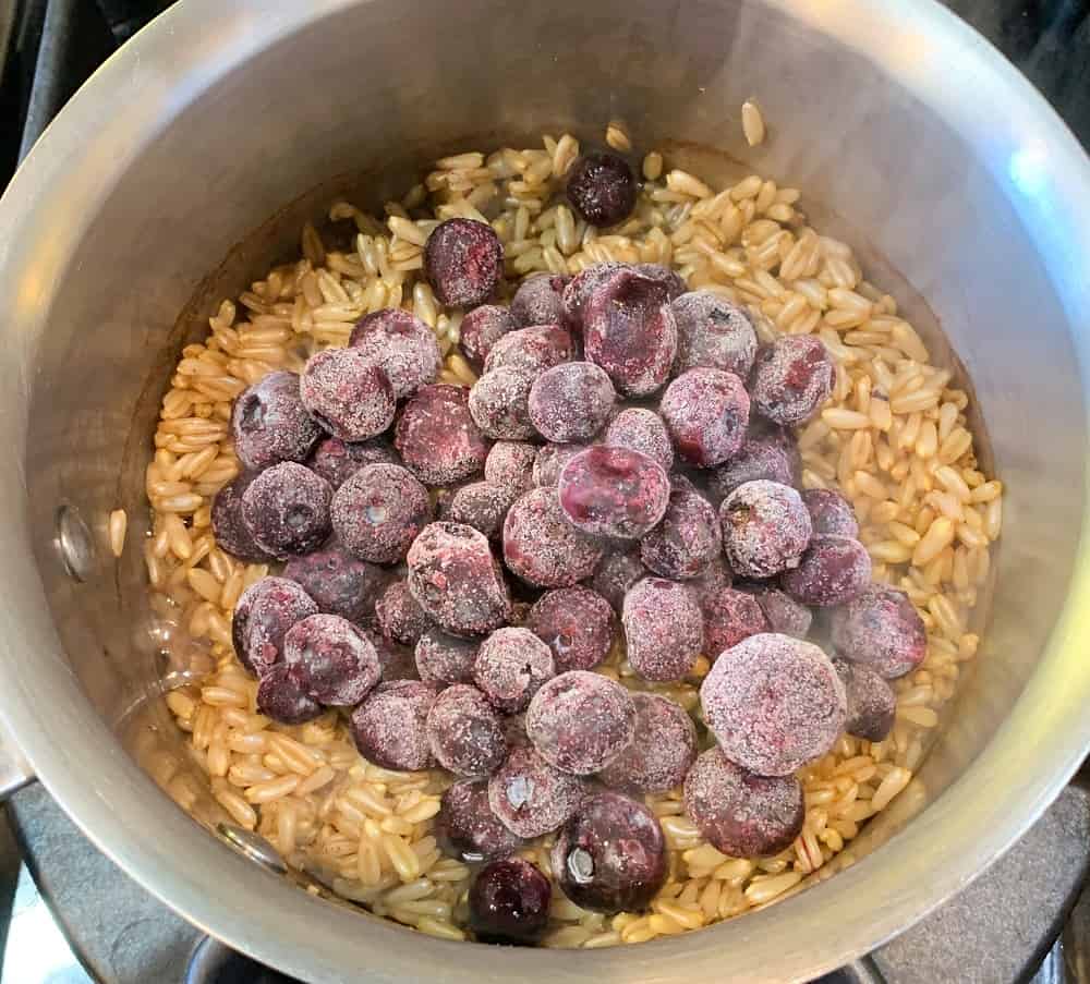 top view and close up of cinnamon oat groats in a pot with frozen blueberries added