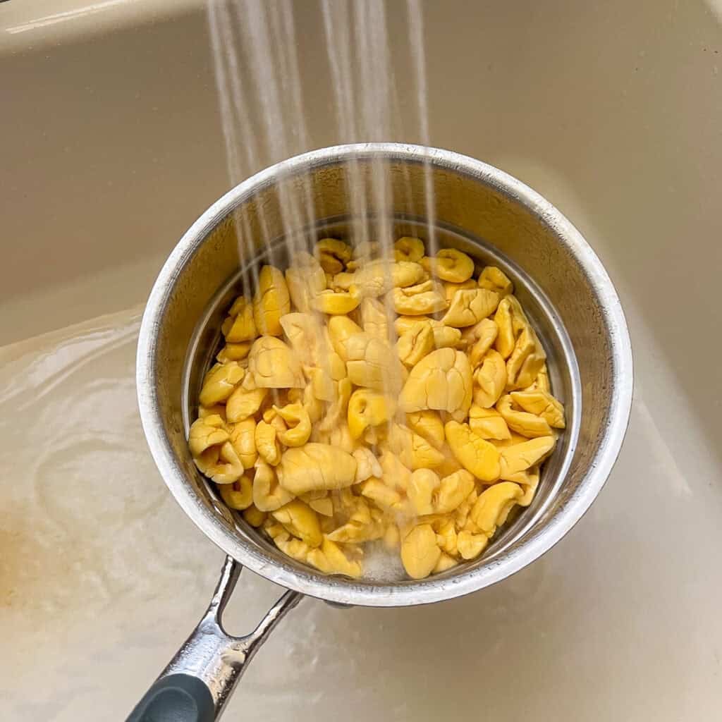 Ackee being drained and rinsed in a colander over the sink.
