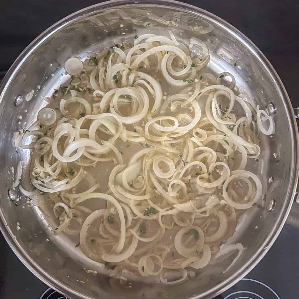 Onions being sauteed in a pan with vegetable broth, thyme, and garlic.