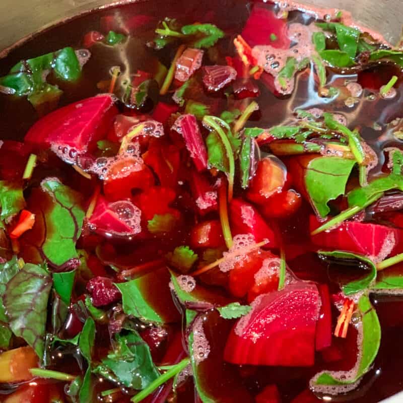 top side close up of beet soup with beetroots, beet greens, cilantro, celery and broth in a stainless steel pot
