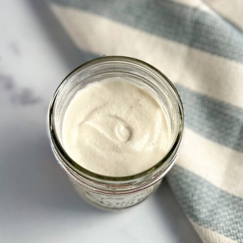 top view close up of a mason jar with cashew sour cream; blue and white stripped napkin on the side