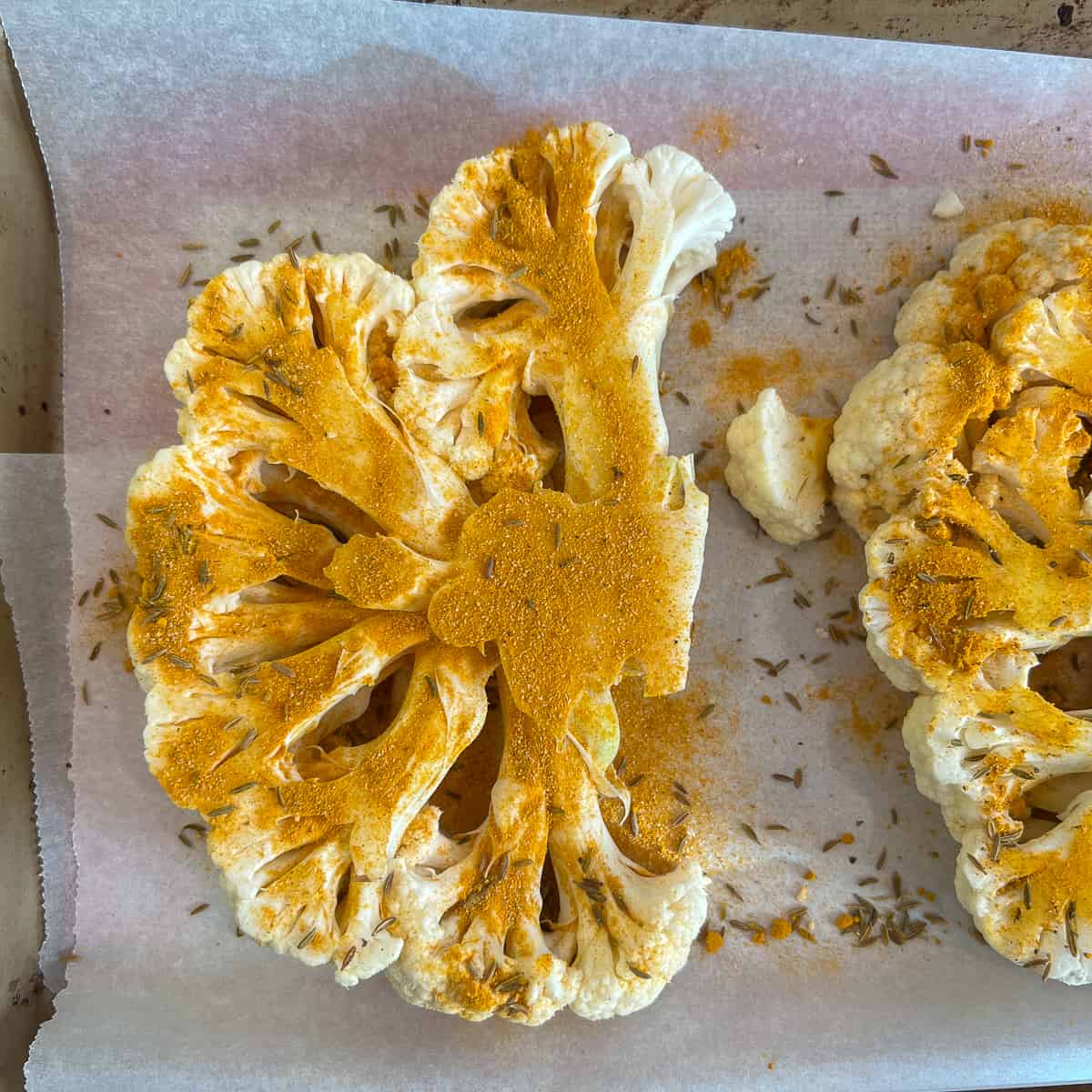 top view of spiced cauliflower steaks on parchment lined baking pan