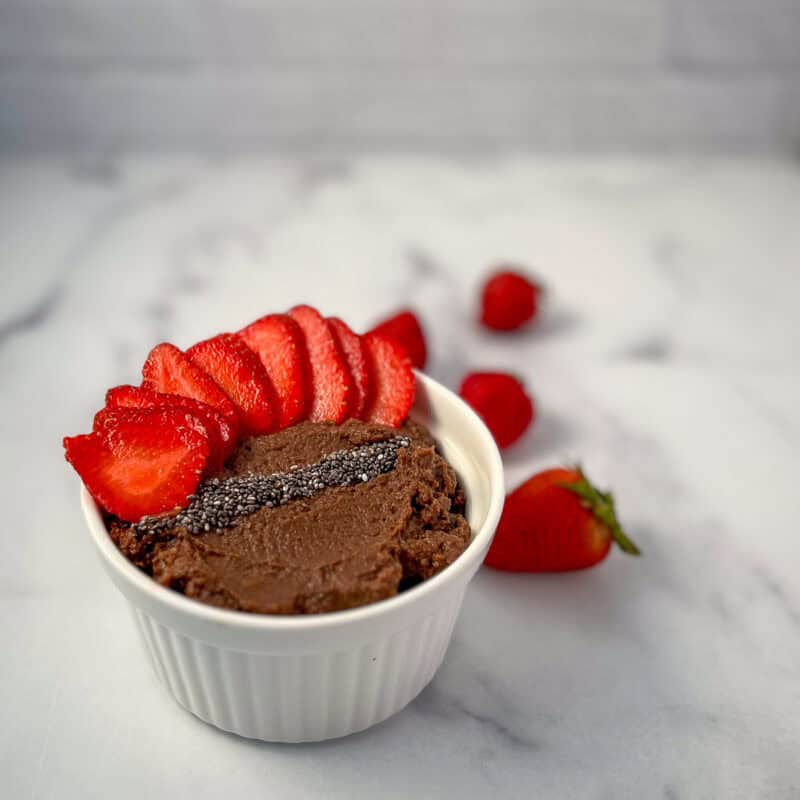 A small bowl of chocolate hummus with fresh strawberries and chia seeds.