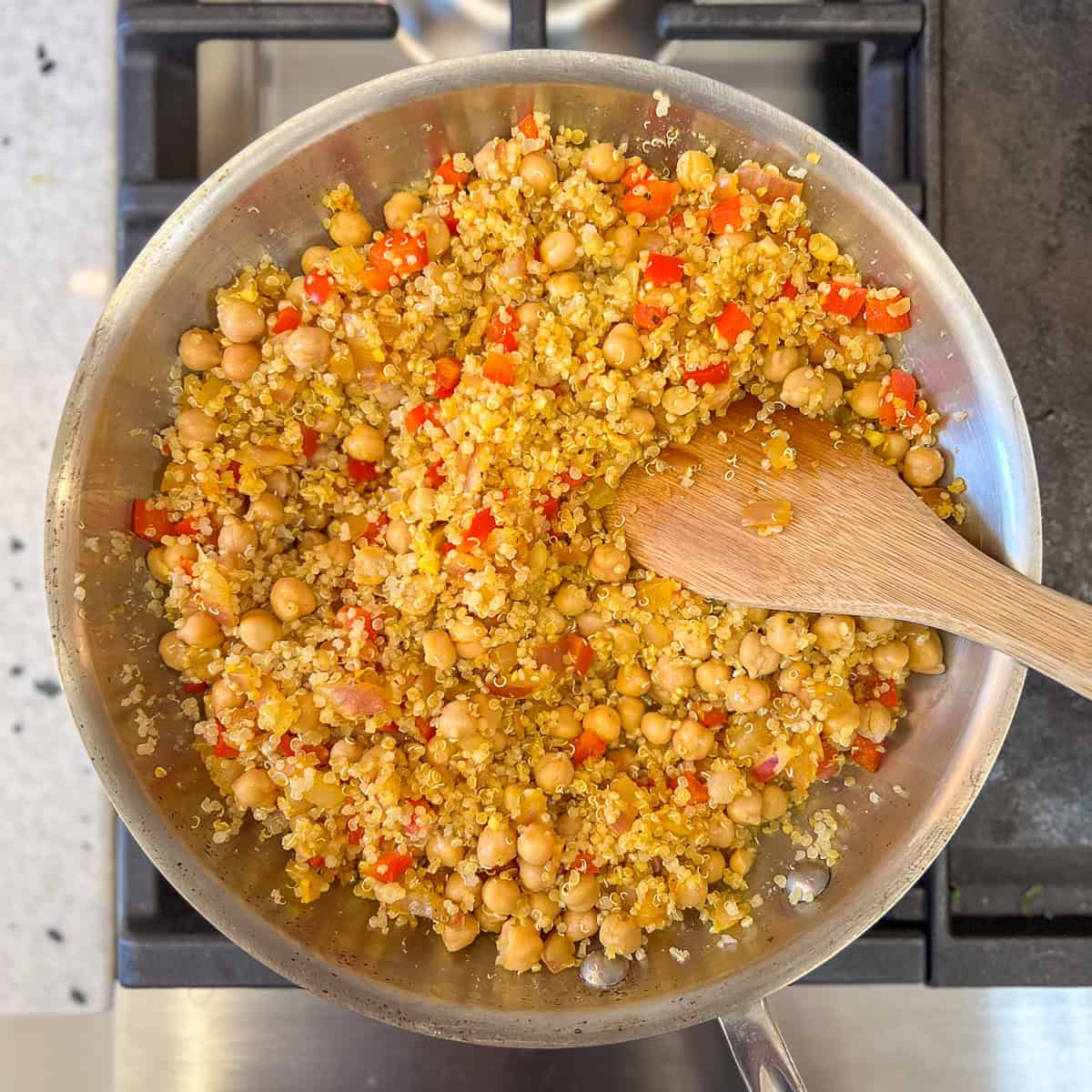 The quinoa chickpea mixture being stirred with a wooden spoon in the skillet.