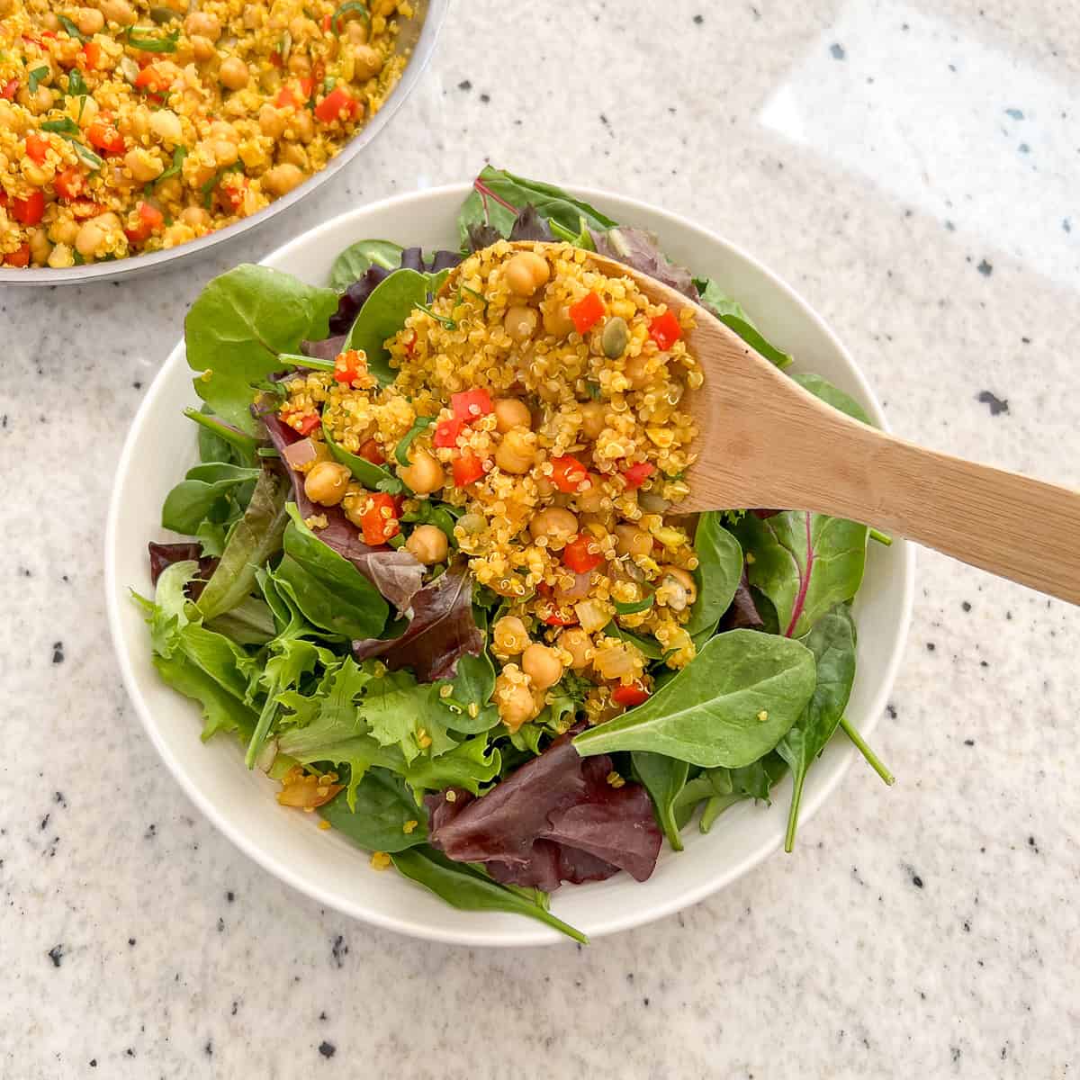 Curry quinoa chickpea mixture being spooned onto a bed of salad greens.