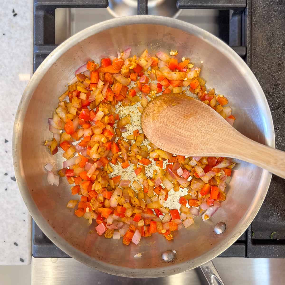 A wooden spoon stirring the minced garlic and curry powder in with the diced onion and bell pepper.