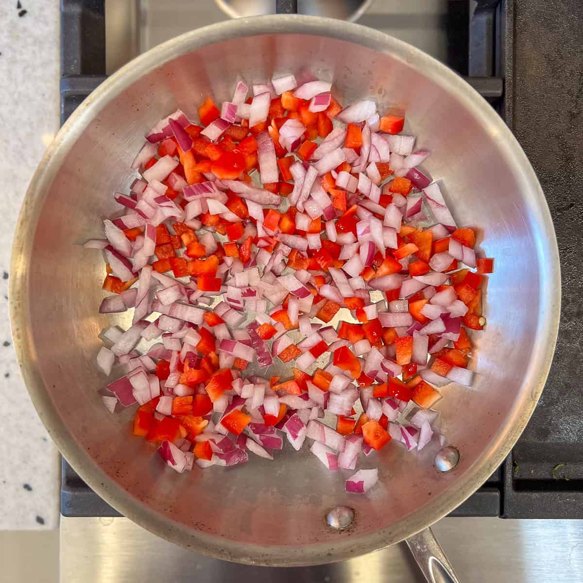 Diced onion and red bell pepper sautéing in the skillet on the stovetop.