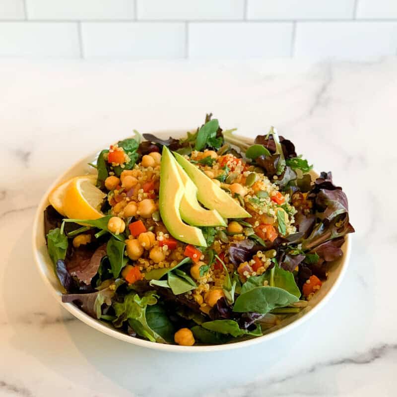 Curry quinoa chickpea salad in a bowl topped with sliced avocado.