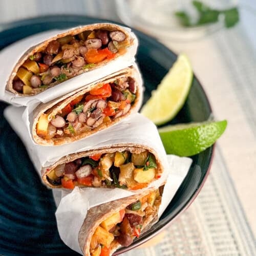 Side view of hearty vegan breakfast burritos stacked on a blue plate with lime wedges