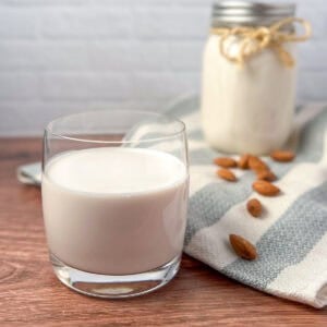 Homemade almond milk in a glass and mason jar; scattered raw almonds on the side.