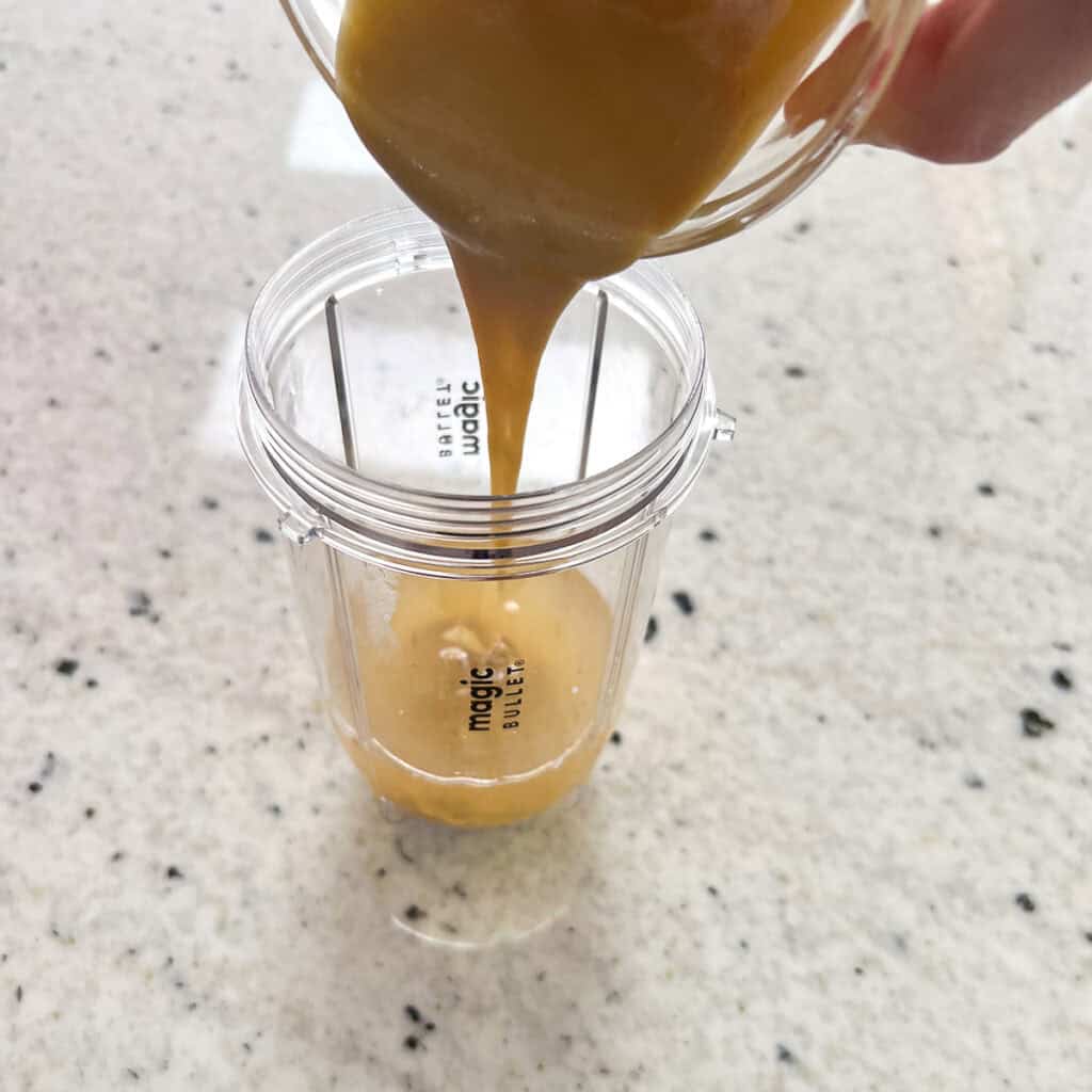 Tahini being poured into the bullet blender cup with other ingredients.