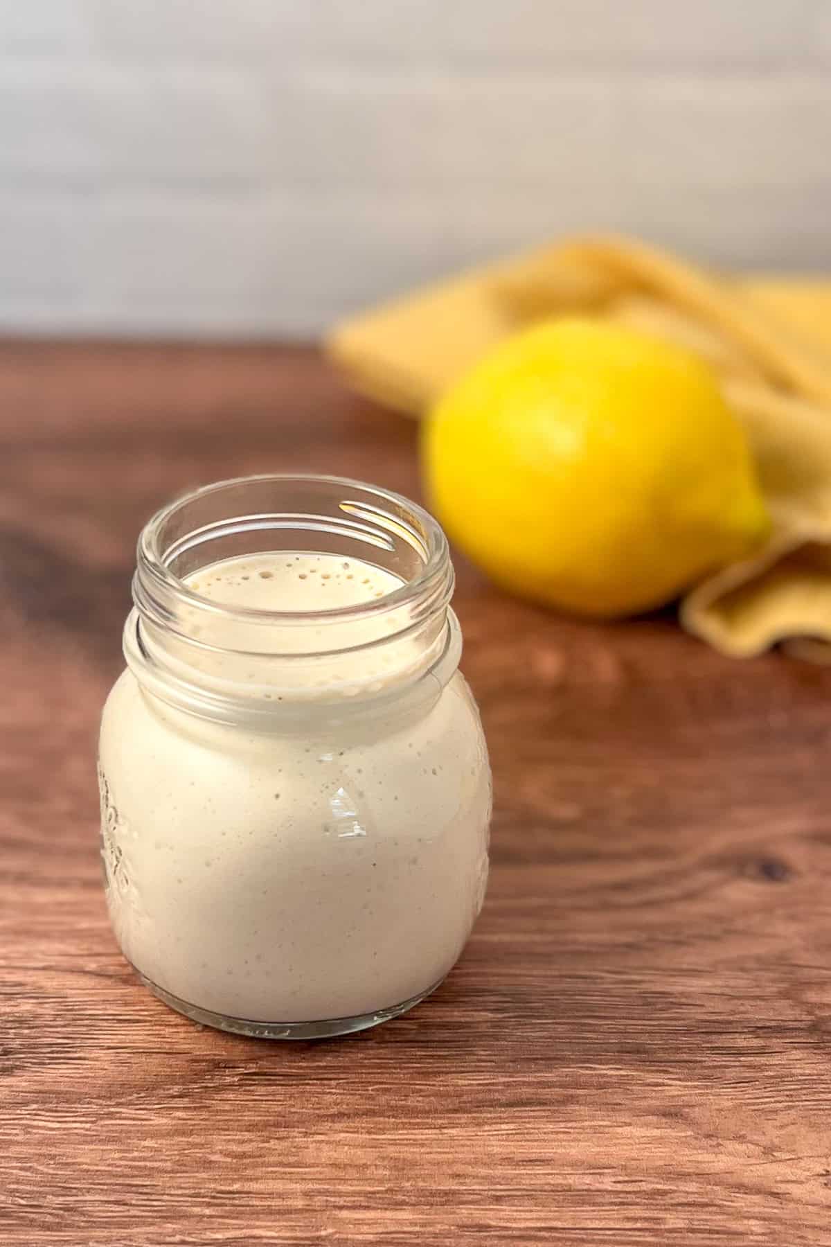 Lemon tahini dressing in a mason jar with lemon in background.