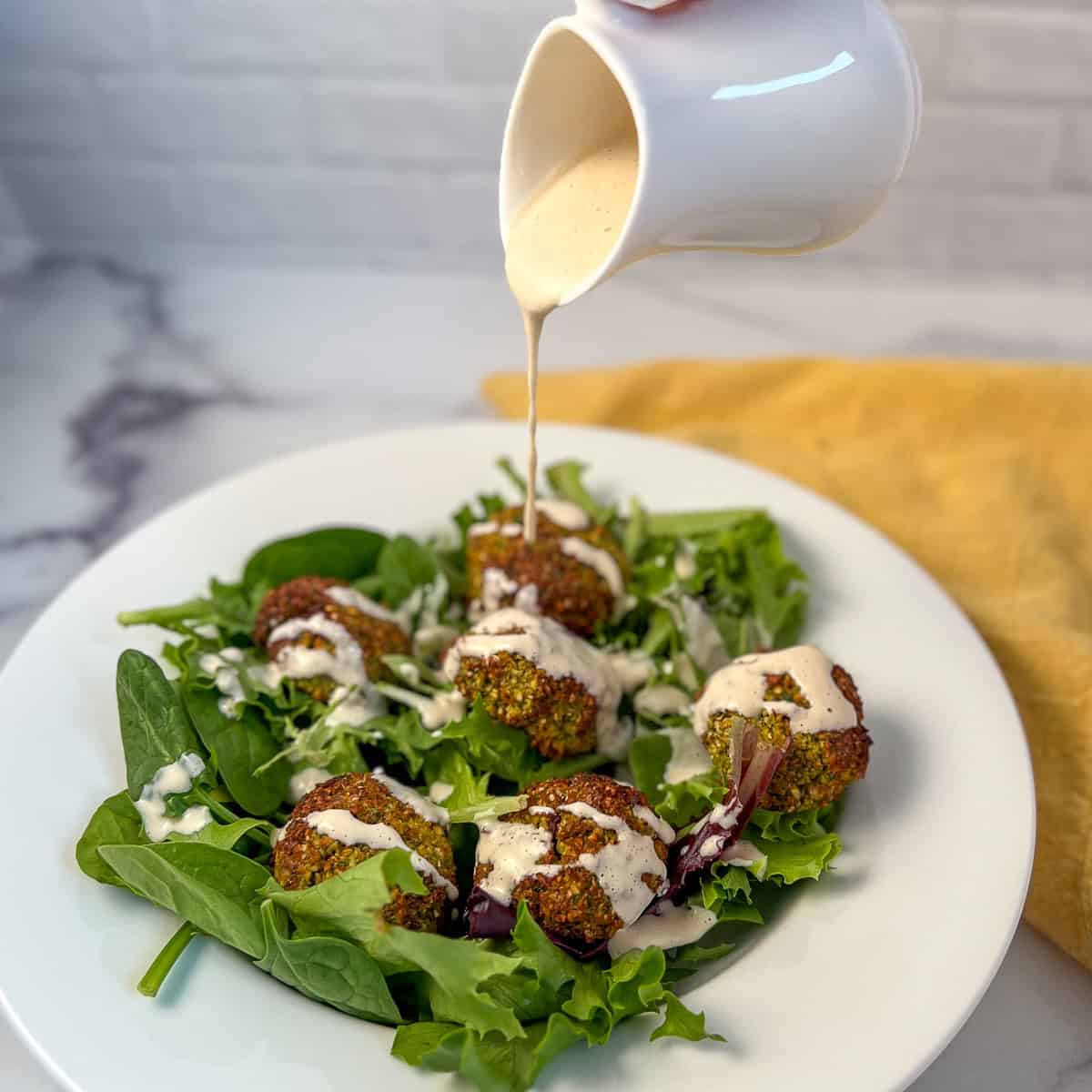 Lemon tahini dressing being poured on a salad with air fryer falafel.