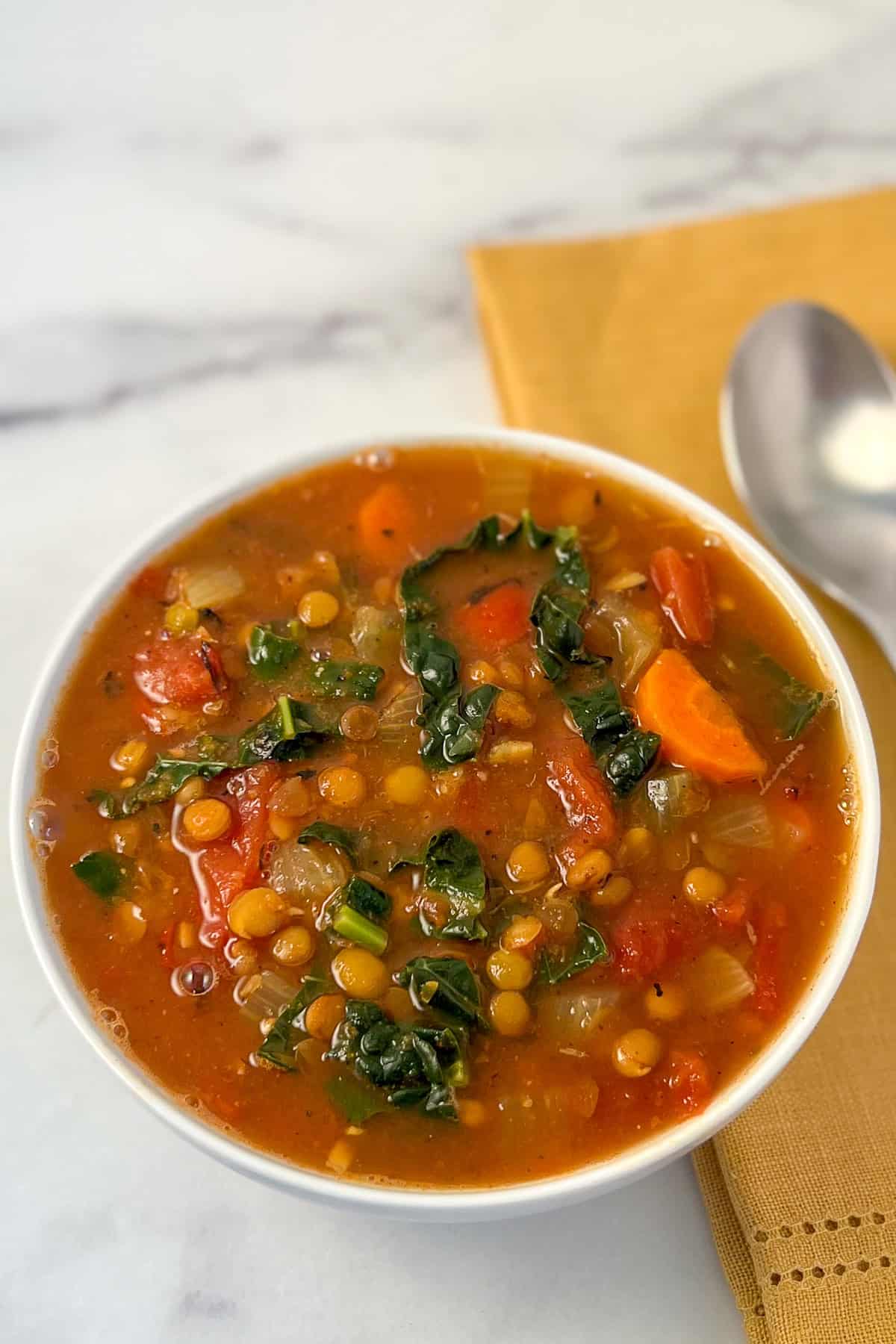 A bowl of lentil soup with spoon and napkin on the side.