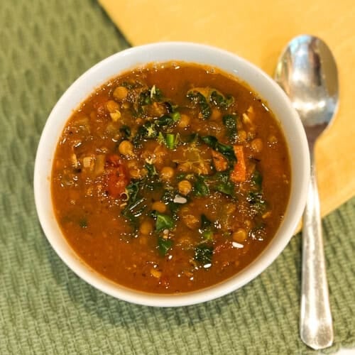 top view of lentil soup in a white bowl with spoon on the side