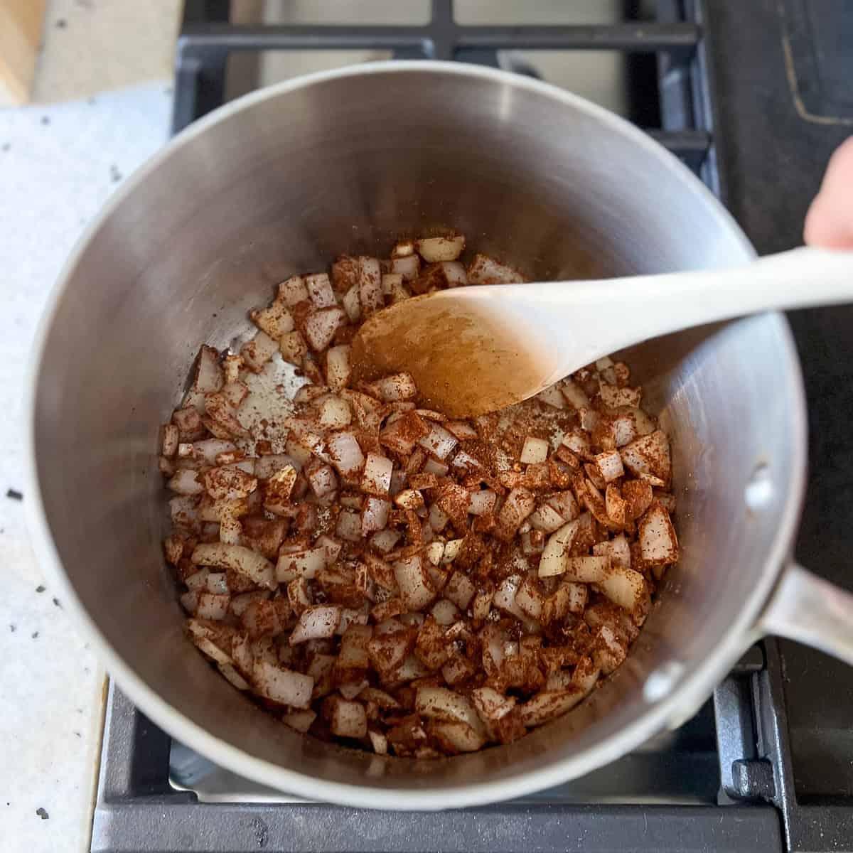 Dried spices being stirred in the pot with chopped onions and garlic.