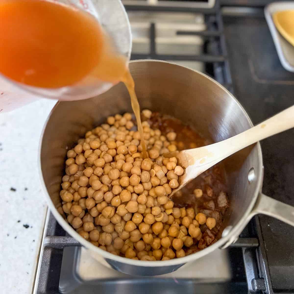 Vegetable broth and chickpeas being added to the pot.