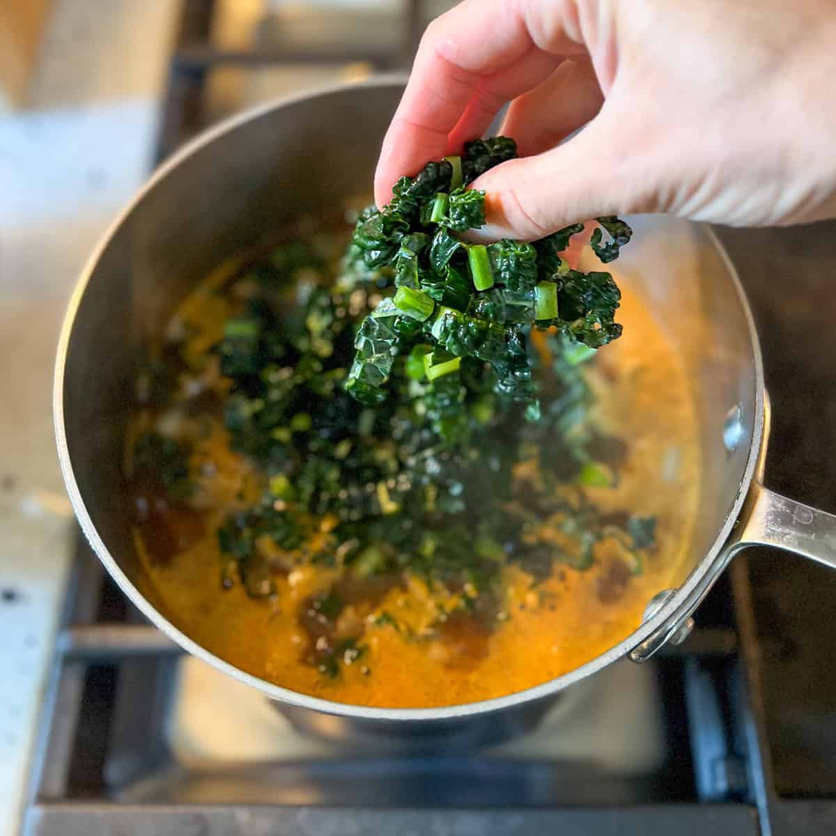 Chopped kale being added to the boiling hot soup pot.