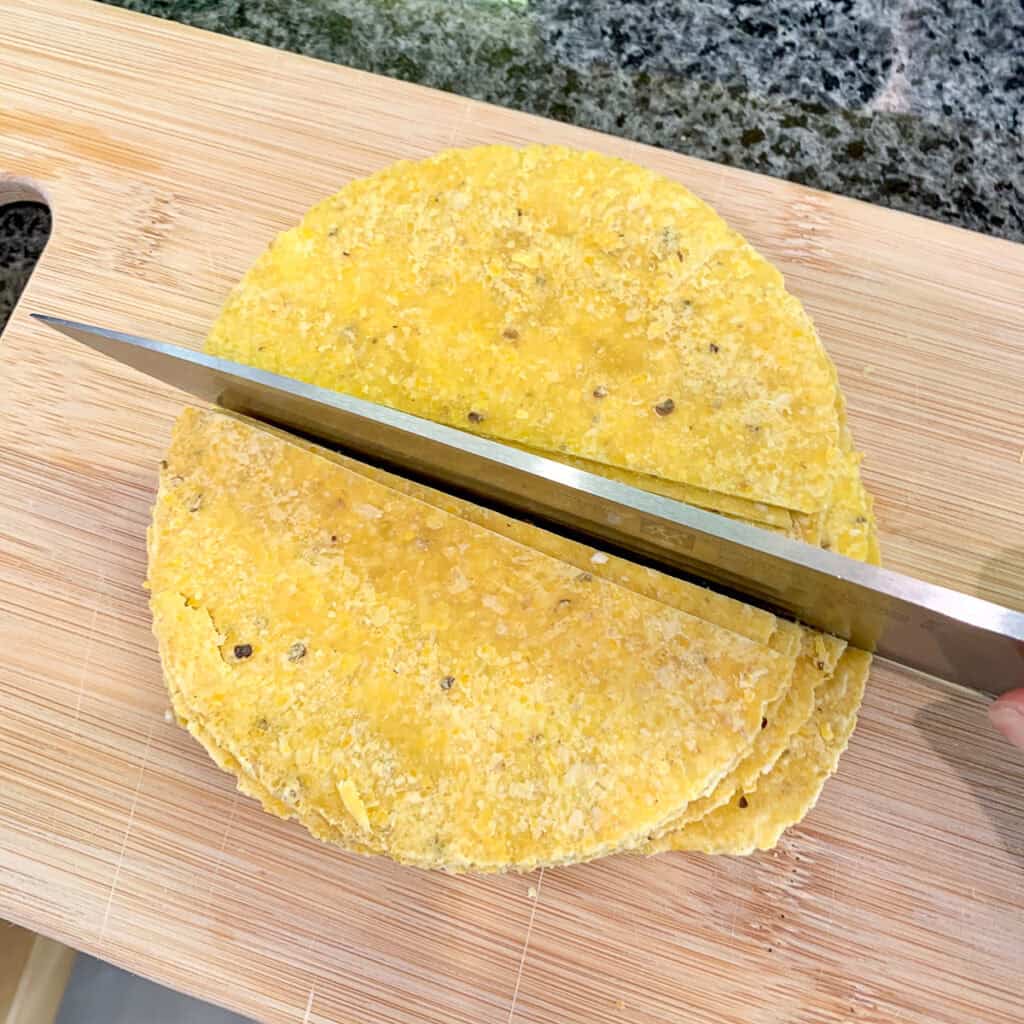 Corn tortillas being cut with a knife on a cutting board.