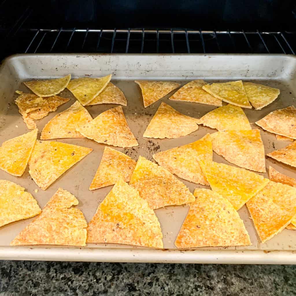 Oven baked corn tortilla chips on a baking sheet after they've crisped up in the oven.