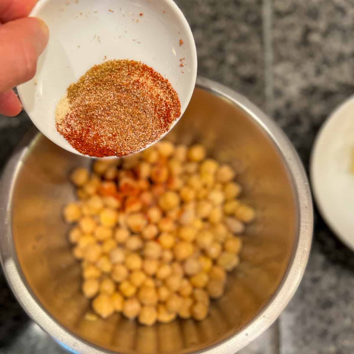 top view of spices being added to chickpeas in a mixing bowl