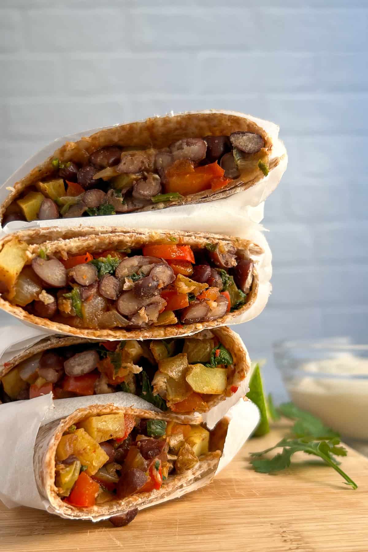 A stack of vegan breakfast burritos on a wooden cutting board.