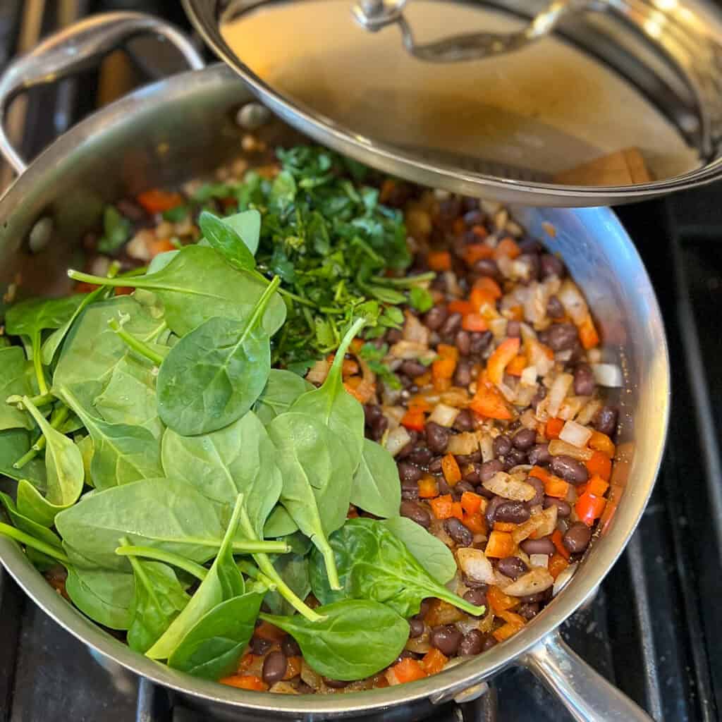 Saute pan with black beans, onions, garlic, bell pepper, spinach and cilantro.