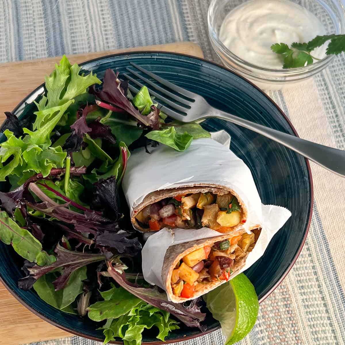 Vegan breakfast burrito on a plate with a simple green salad and fresh lime.