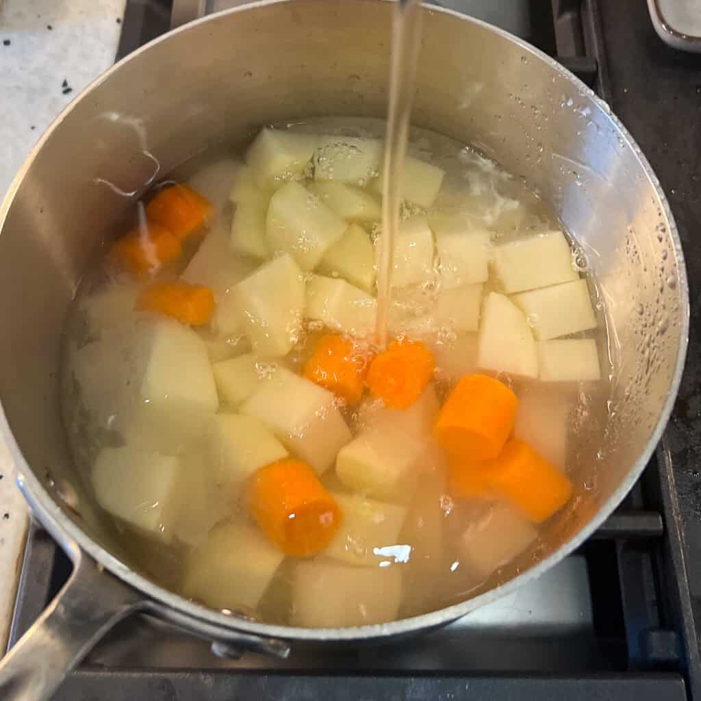 Potatoes and carrots in a pot with water on the stovetop.