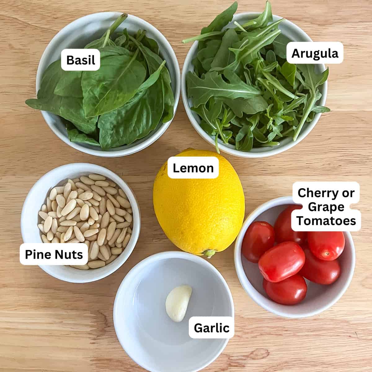 Ingredients for arugula basil pesto sauce: fresh basil, arugula, cherry tomatoes, pine nuts, lemon and garlic.