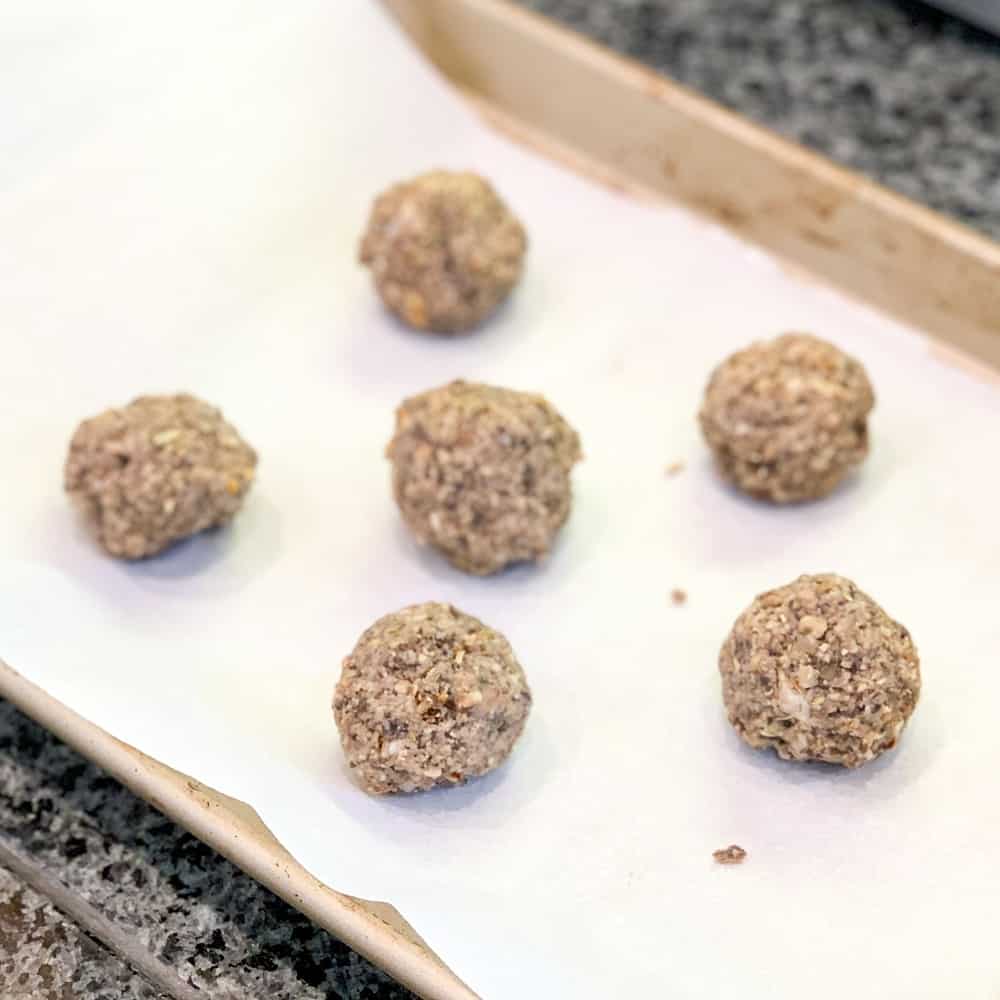 a baking sheet lined with parchment paper and six magic meatballs lined up ready to go into the oven