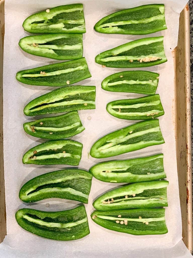 sheet pan lined with parchment paper and 8 jalapenos sliced in half with seeds removed, lined up.