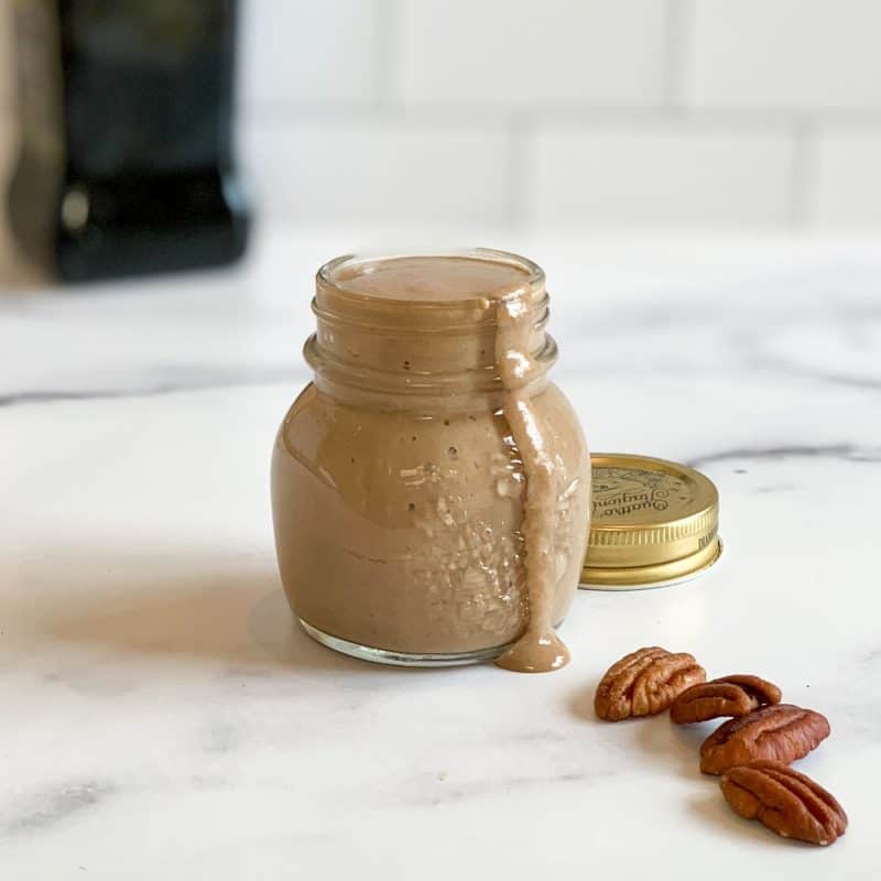 a clear jar with pecan balsamic vinaigrette dressing on a marble surface and pecan halves in front